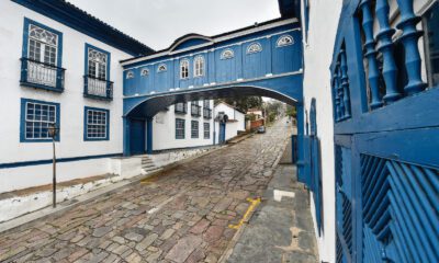 Rua de pedras, com casaria e passadico, pintados em branco e azul.