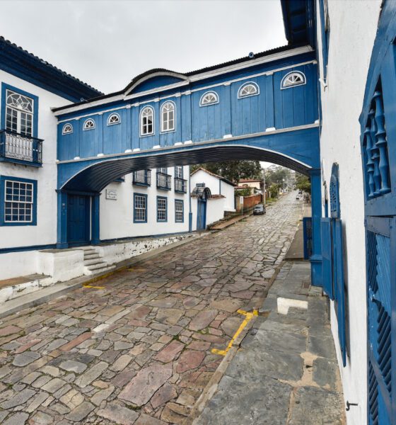 Rua de pedras, com casaria e passadico, pintados em branco e azul.