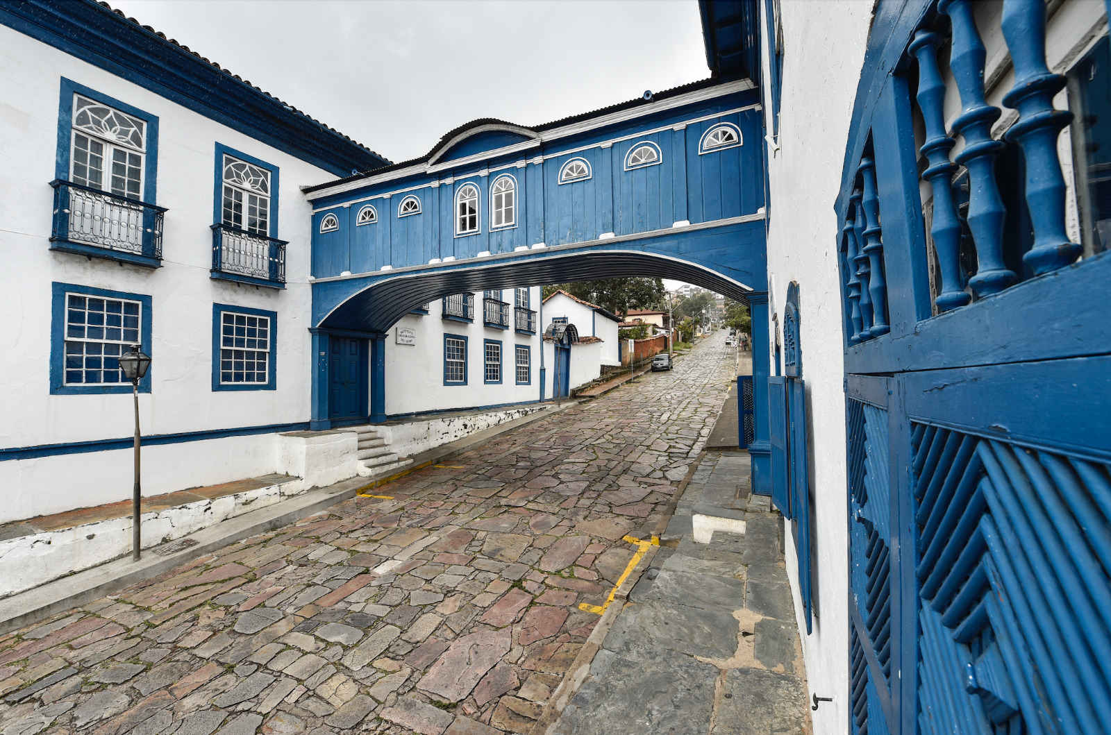 Rua de pedras, com casaria e passadico, pintados em branco e azul.
