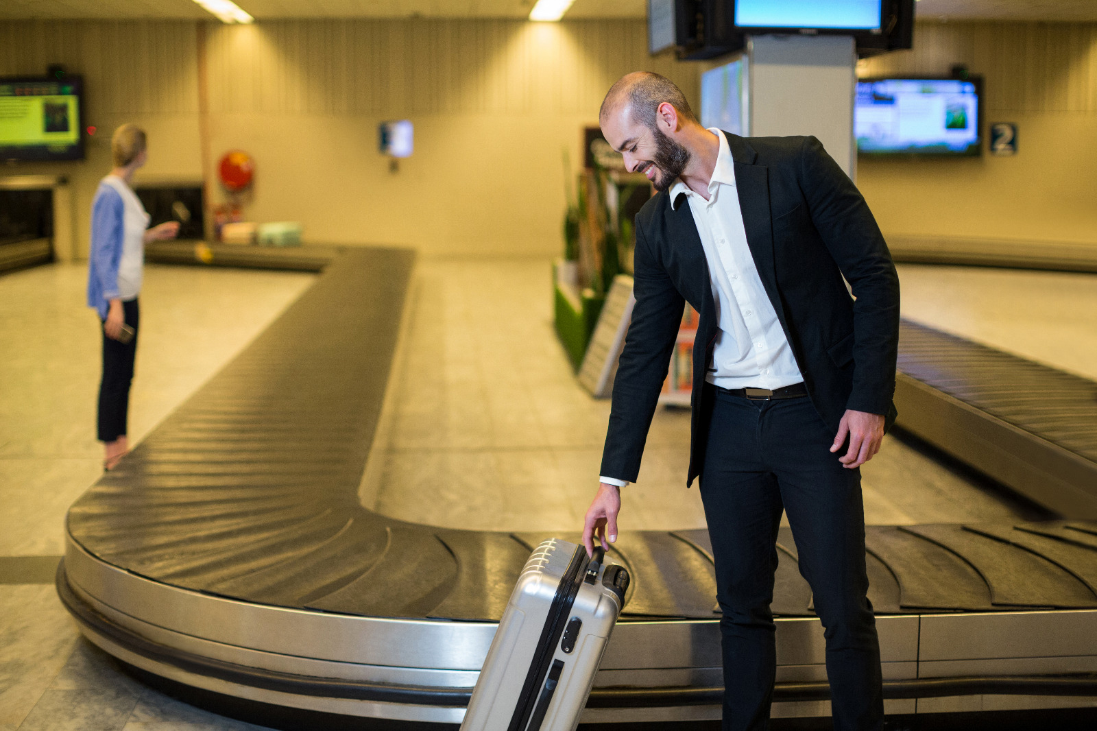Homem sorridente pega mala na esteira do aeroporto