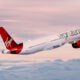 Foto de avião branco e vermelho com a marca Virgin Atlantic, sobe as nuvens.