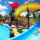 Parque aquático com toboáguas azuis, piscina e crianças escorregando
