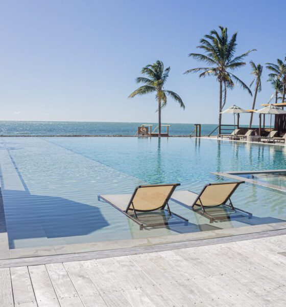 Piscina com duas espreguiçadeiras beges dentro e com vista para o mar