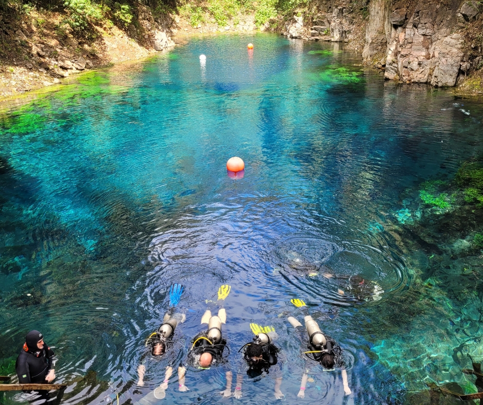 Lagoa misteriosa com água muito azul e mergulhadores com cilindros